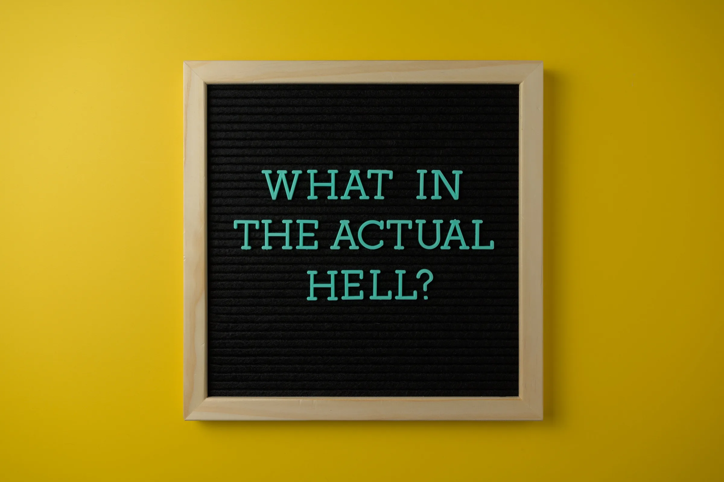 Letter board with humorous quote 'What in the actual hell?' on a vibrant yellow backdrop.